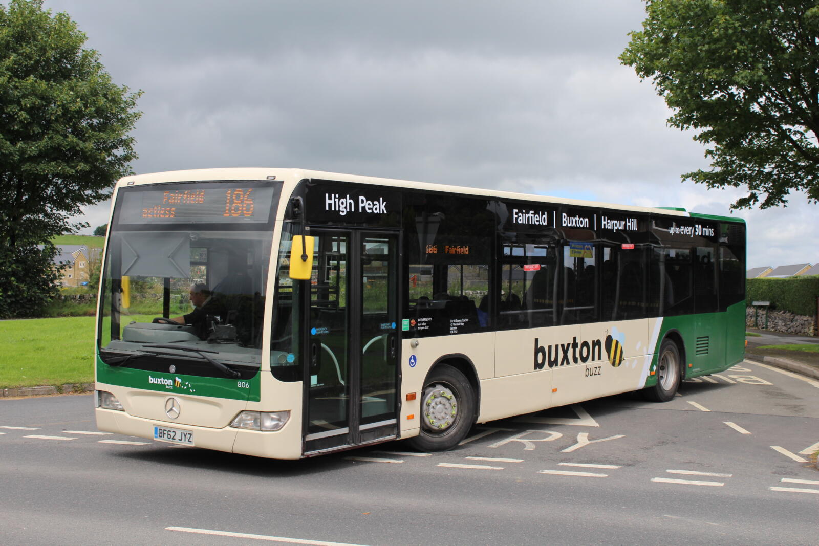 A beige and green bus at a junction next to an area of grass