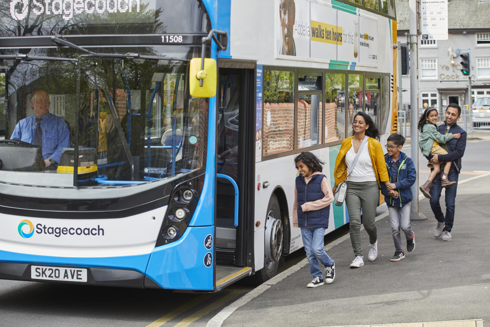 a blue and white bus with a family of 5 approaching to board, the father holding the smallest child